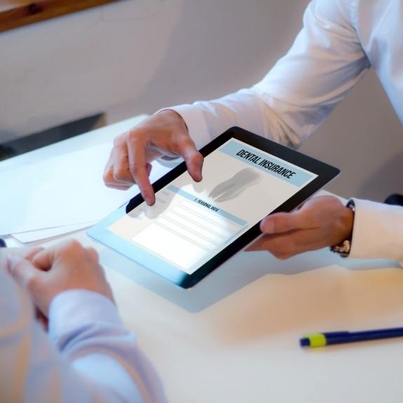 Two people sitting at desk looking at dental insurance information on tablet