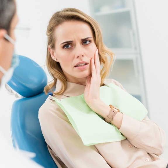 Woman holding her cheek in pain while talking to dentist