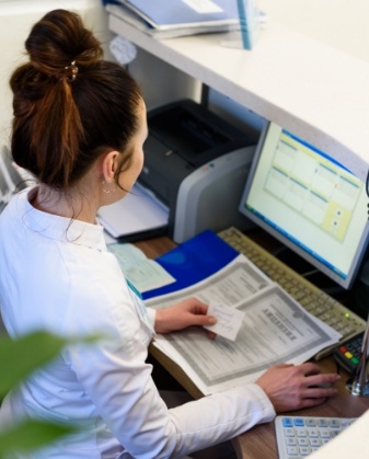 Woman with several paper forms typing on computer