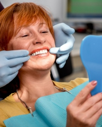 Older woman in dental chair admiring her smile in mirror