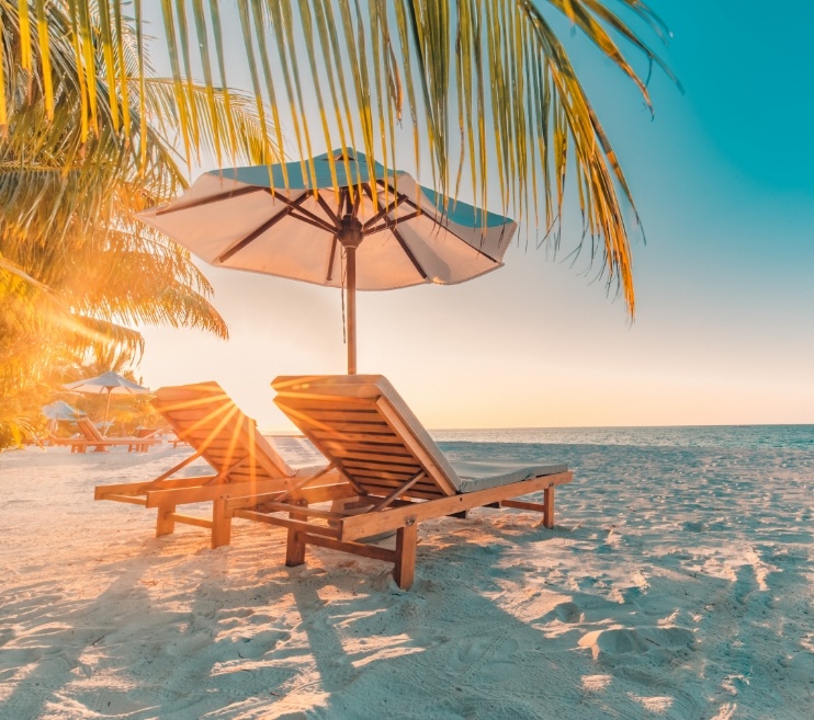 Two wooden chairs with umbrella on beach at sunset