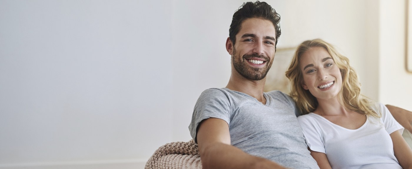 Smiling man and woman sitting on couch after periodontal services in Cranford