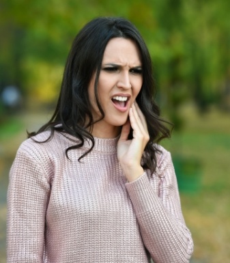 Woman in sweater holding her cheek in pain